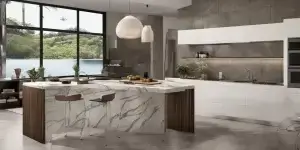 Cozinha gourmet espaçosa com ilha central de mármore branco, armários de madeira escura, e área de convivência com sofá cinza claro e mesa de centro de vidro.