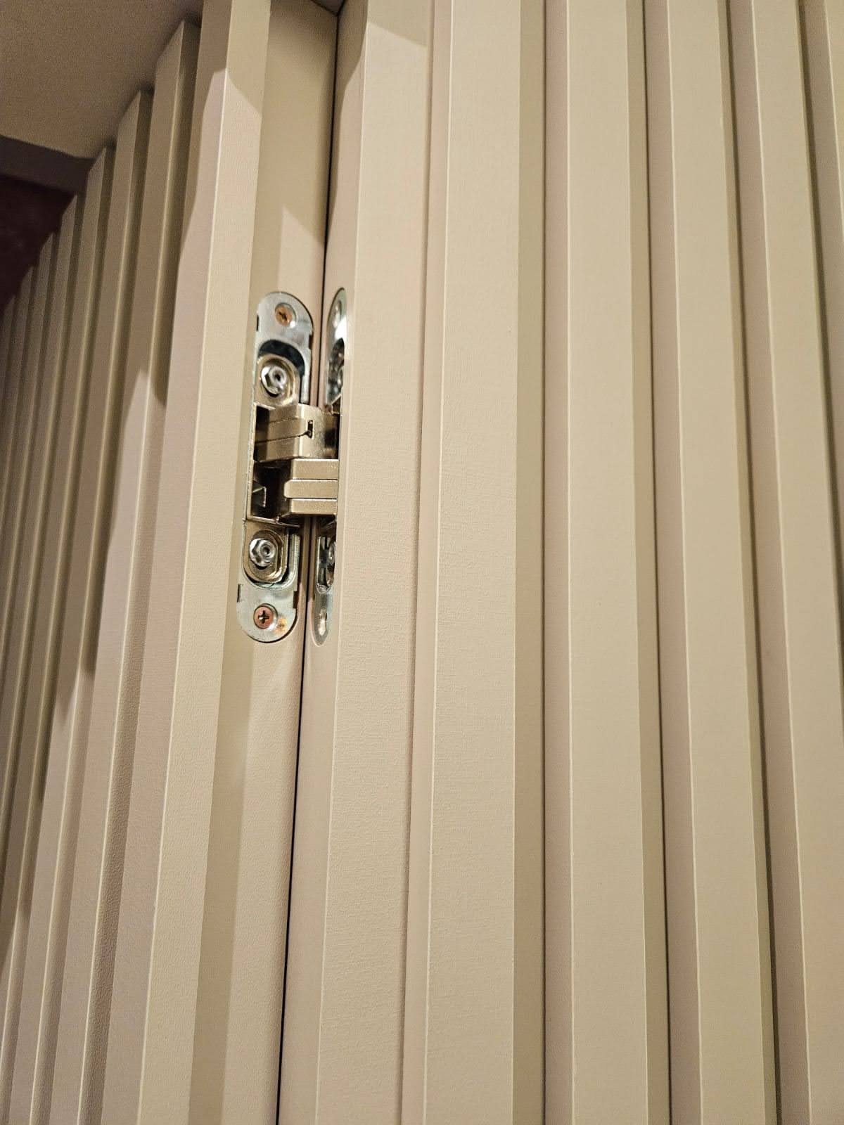 Exemplo de porta mimetizada embutida no painel de MDF na sala - detalhe da dobradiça